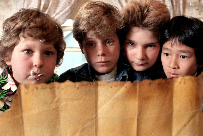 Four kids holding an old parchment map indoors with creases and discoloration.