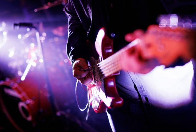 A close up of a musician playing his electric guitar with a band in the background