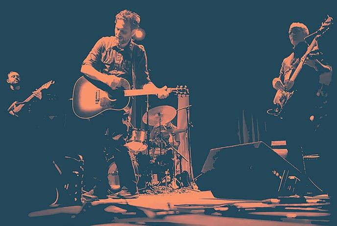 A sepia-toned image of the band Great Lake Swimmers performing live, with the lead singer playing an acoustic guitar.