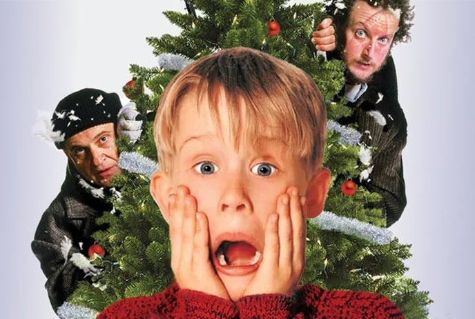 Macaulay Culkin looking surprised in front of a Christmas tree, with the two villains from the movie in the background.