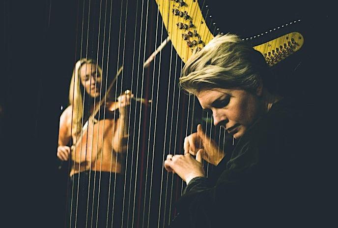 Aoife Ní Bhriain plays the fiddle in the background while Catrin Finch focuses intently on her harp during a performance.