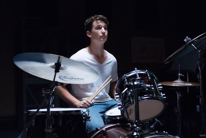 A Person playing a drum set in a dimly lit room, creating a moody, artistic atmosphere wearing a white shirt and blue jeans.