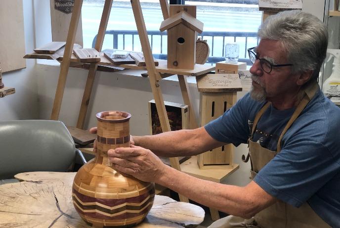 Person sitting at a table forming a wooden object.