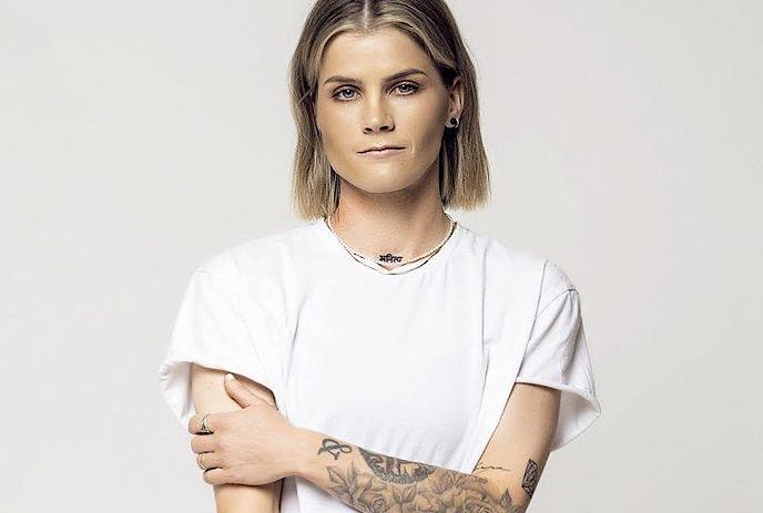 A woman with tattoos, in black tank top, posing for the picture with a black and white background setting.