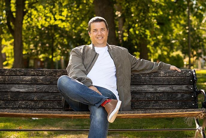 A person sits cross-legged on a park bench with smiling face, surrounded by lush greenery, enjoying a peaceful moment.