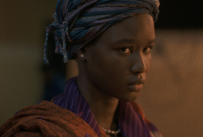 Young black person wearing a head covering, looking at the camera.