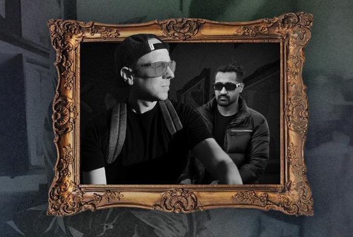 Two men dressed in dark clothing and sunglasses are framed by an ornate, vintage-style picture frame.
