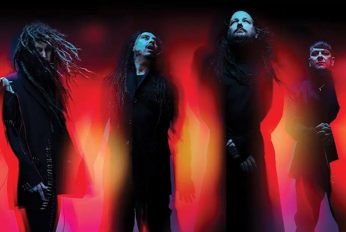 Four members of the band Korn stand together, dressed in dark clothing.