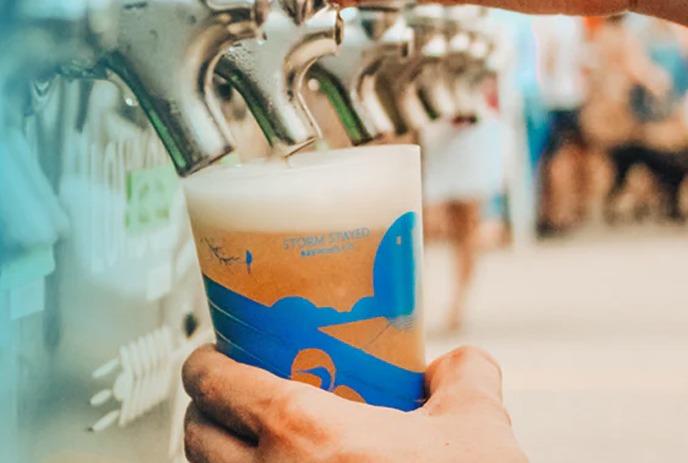 A hand holding a glass with a colorful illustration of a sunset on the water.