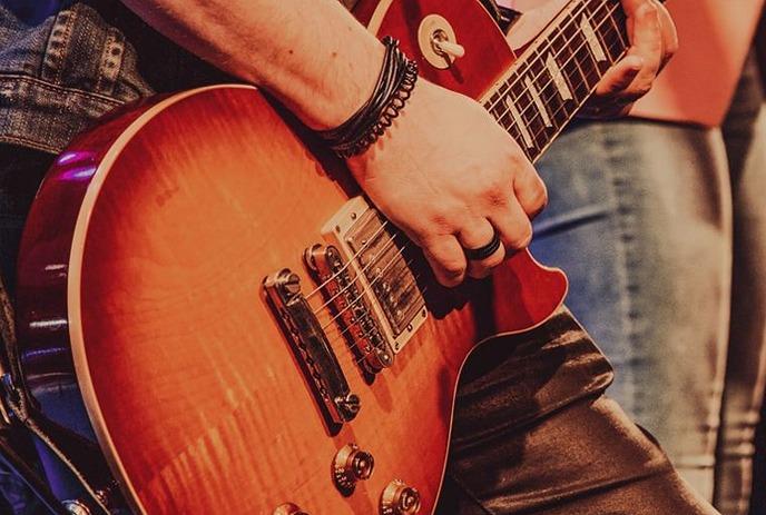 A male playing an orange electric guitar on the stage while wearing a denim jacket.