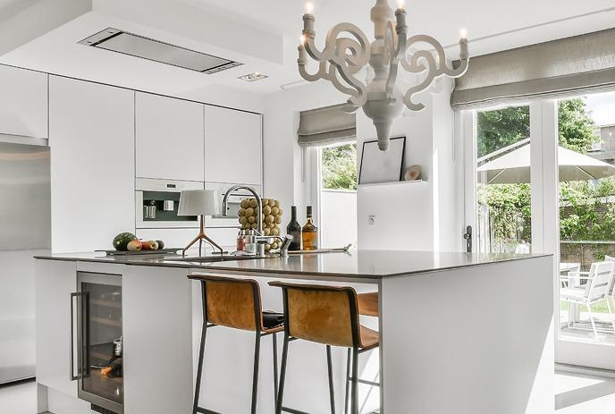 A modern kitchen with a central island, a large potted plant, wooden stools, and pendant lights.