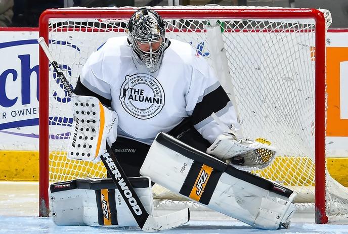 A hockey player in a white and black uniform with a hexagonal logo featuring the number 25, skating on the ice.