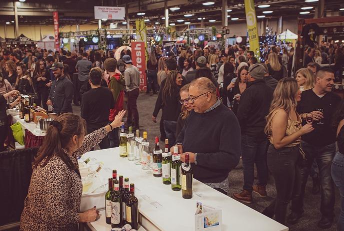 Attendees gathered at the London Wine & Food Show, enjoying wine and food from various booths and a wooden bar setup.