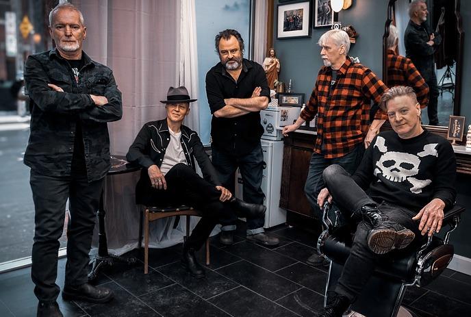 The band Lowest of the Low poses casually inside a barber shop, surrounded by vintage decor and barber equipment.