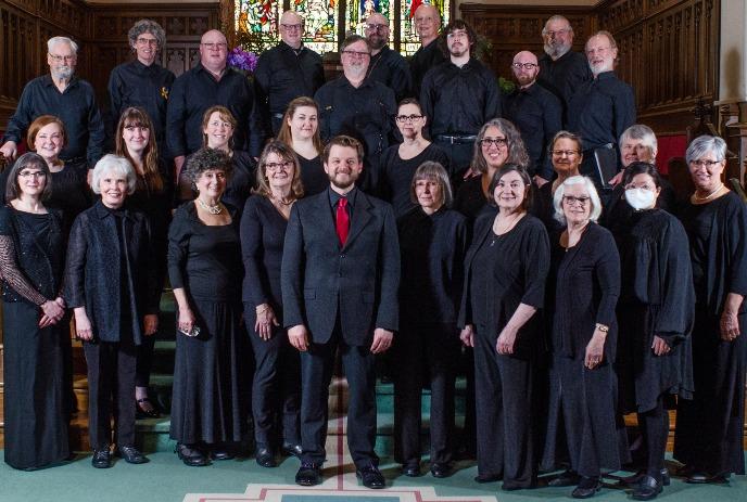 A group of people dressed in black formal attire standing in rows inside a church with stained glass windows in background.