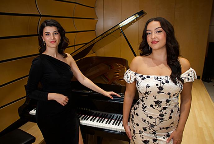 Two people standing in front of a grand piano in a studio.