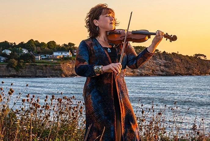 Lucy MacNeil gazes at a sunset on a coastal cliff, violin in hand.