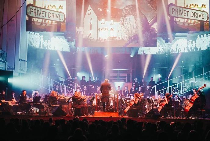 An orchestra seated on stage with lights shining on images behind them.