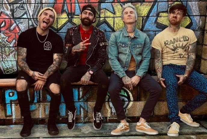 Four male members of the band MEST sit on a ledge against a colorful graffiti wall.