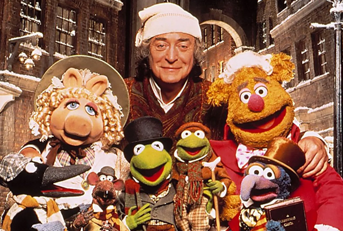 A group of Muppet characters, including Miss Piggy and Kermit, dressed in Victorian clothing, pose with a person.