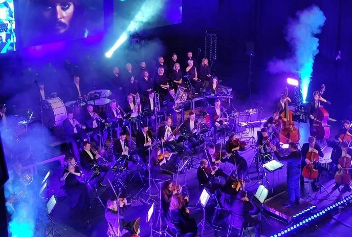 A full orchestra on stage under purple and blue lights.