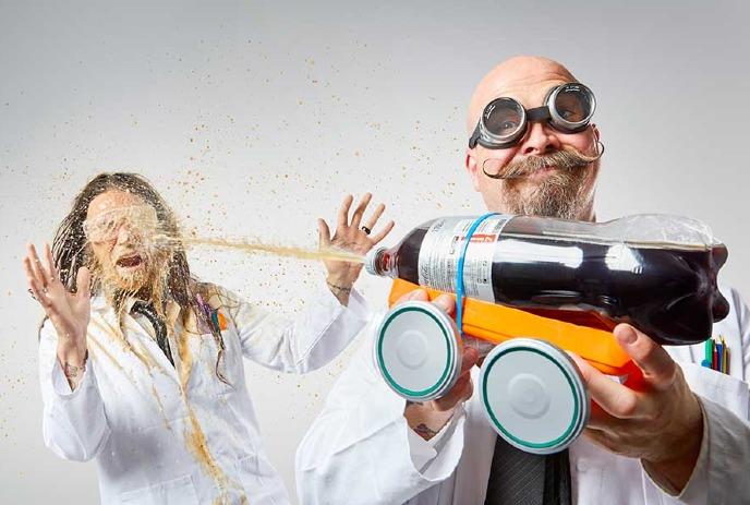 Prof. Burnaby Q. Orbax sprays soda from a soda bottle rocket onto lab assistant Sweet Pepper Klopek.