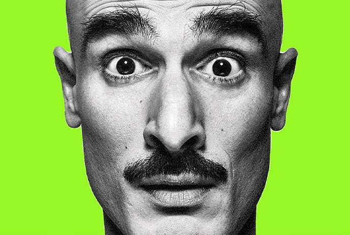 A man with a surprised expression and a mustache shown in black and white on the left side, with a bright green background.