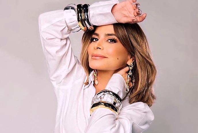 Paula Abdul posing for the camera in front of a white background, wearing a black dress.