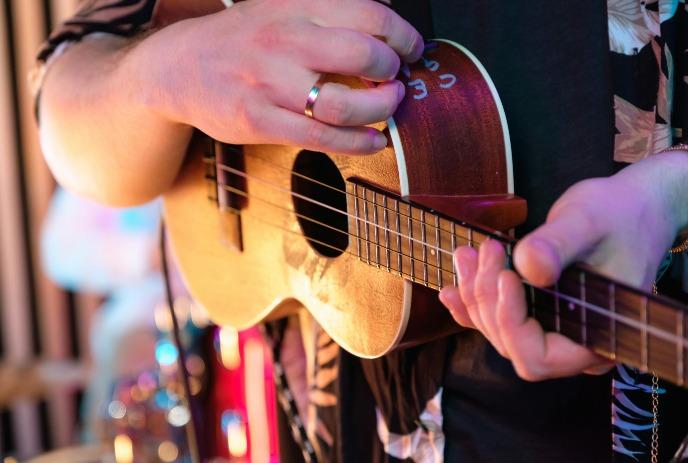 A close-up picture of a person playing a brown ukulele with a blurry background.