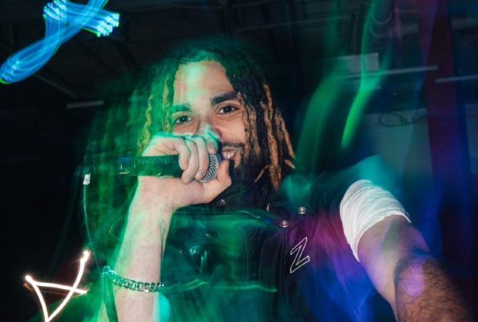 A man holds a microphone, performing in a dimly lit setting, with vibrant neon streaks and motion blur around him.