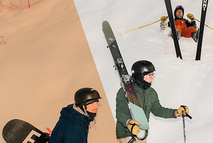 One person lying in the snow with their skis up, two people walking past with their ski equipment.