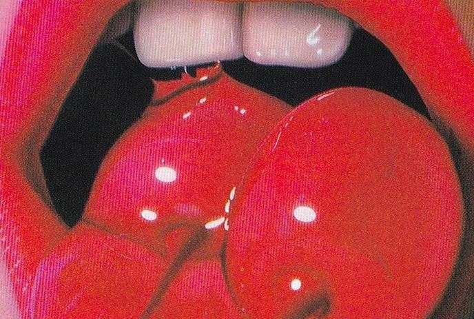 A close-up of a woman’s lips, painted in vibrant red, with a glossy finish, against a plain background.