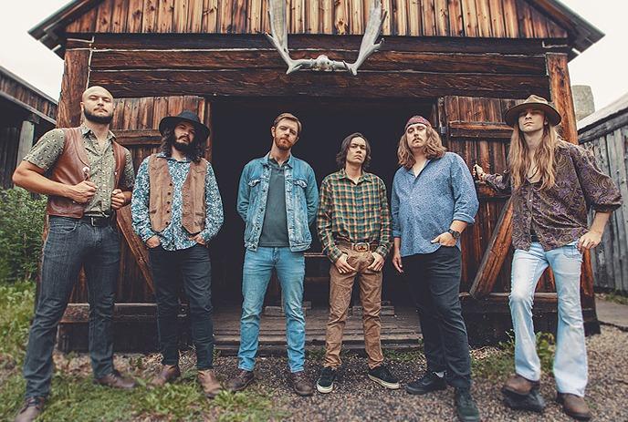 The band Sparrow Blue standing in front of a cabin made from wood