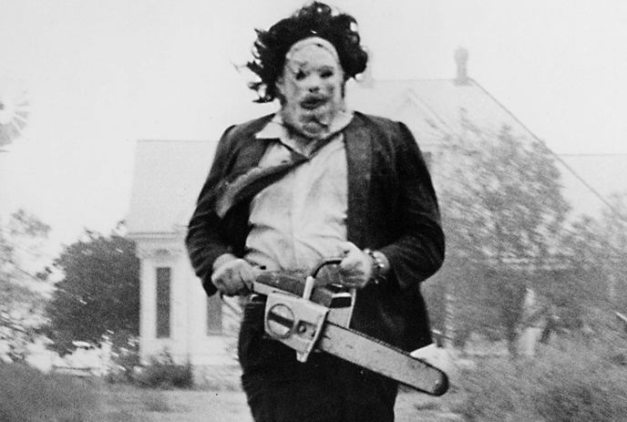 A guy holding a chainsaw in a suite, eerie atmosphere and dense trees in the background.