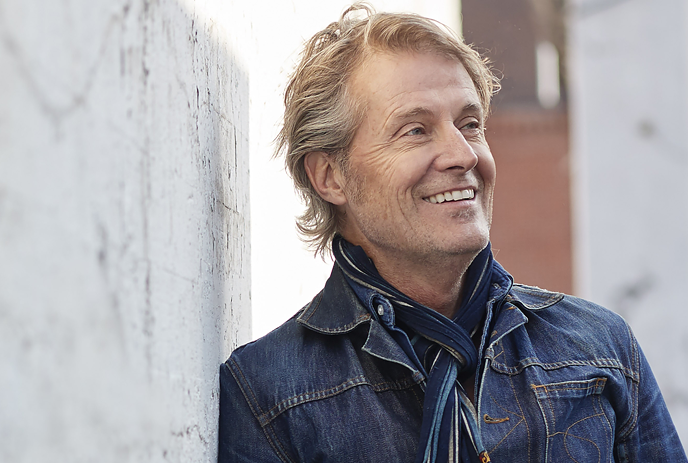 Jim Cuddy smiling while leaning on a wall.