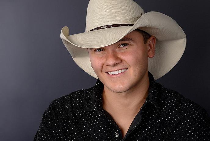 A person smiling in cowboy hat, maple leaves and wooden board in the background.