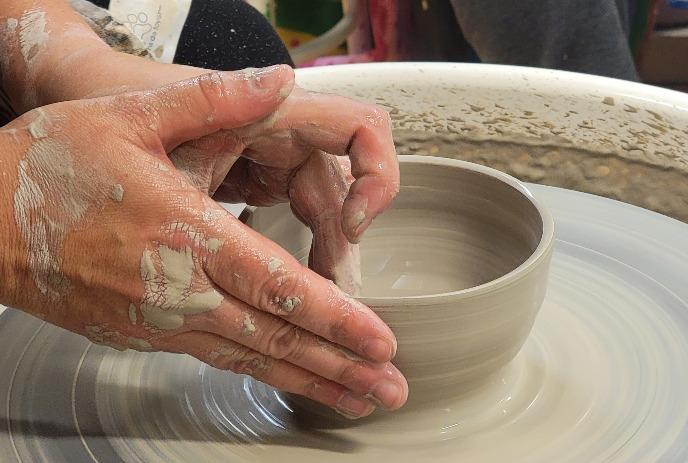 Hands shaping a wet clay pot on a spinning potter’s wheel.