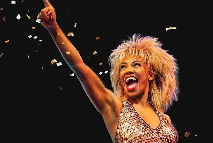 The woman playing Tina Turner in the musical performing on stage, with backup dancers in the background.