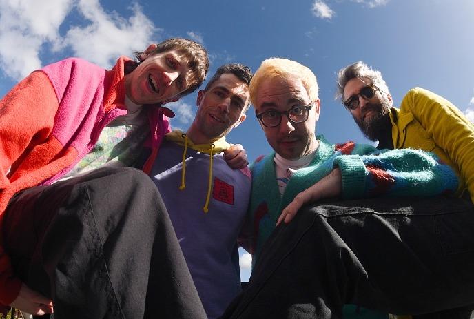 The 4 band members of Tokyo Police Club posing for the camera outside, with a blue sky in the background.