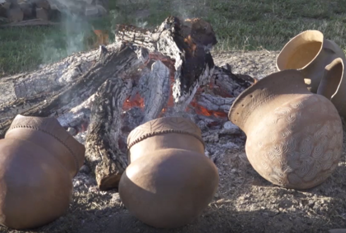 Four intricately designed clay pots are placed near an open wood fire, showcasing traditional craftsmanship.