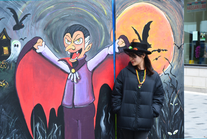 A person stands in a vibrant street mural depicting Halloween themes, including bats and a character dressed as Dracula.