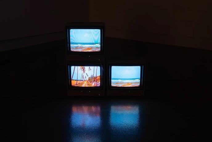 Three vintage CRT televisions stacked, each displaying a beach scene.