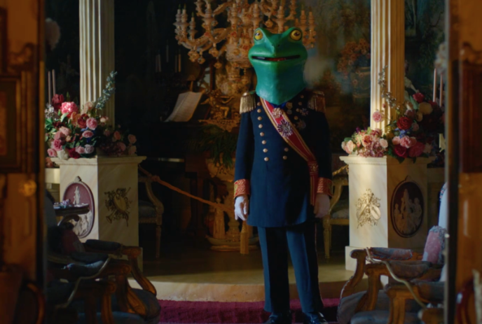 Person in a castle wearing a uniform with a green frog head covering their face.