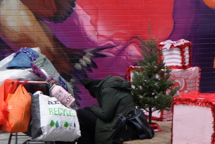 A person sitting in Market Lane with their belongings, and a painted mural in the background.