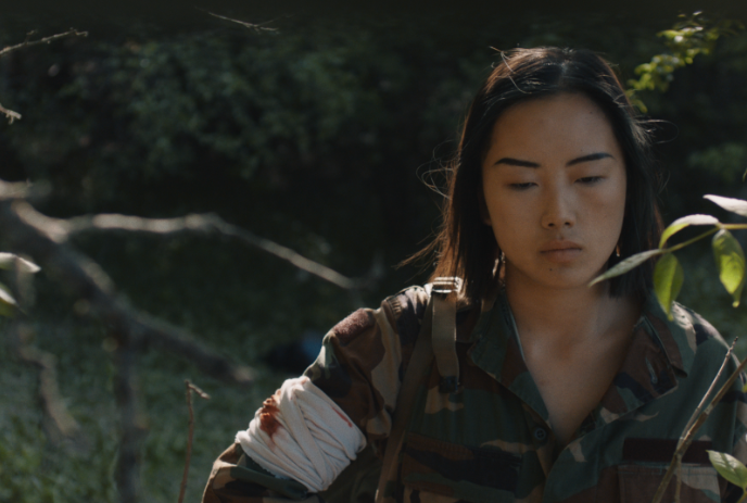 Person wearing camouflage clothing with a wounded arm walking through the woods.