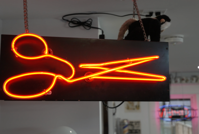 Neon sign with orange scissors and a monkey sitting on top.