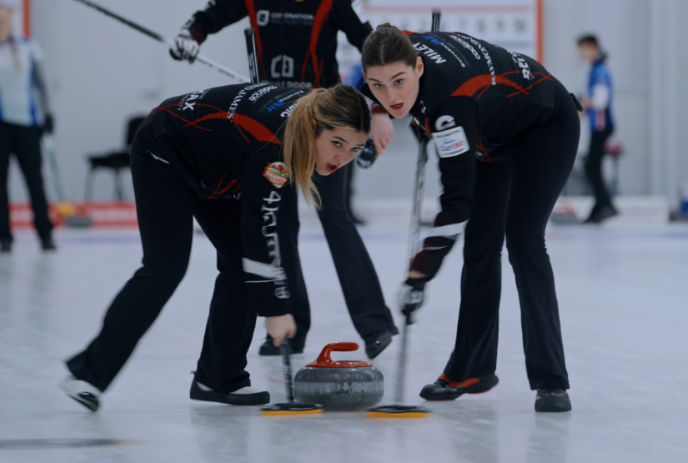 Two people sweeping a curling rock as it goes down the rink.