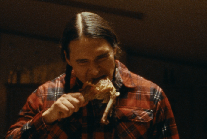 Person wearing plaid jacket eating a large turkey leg.