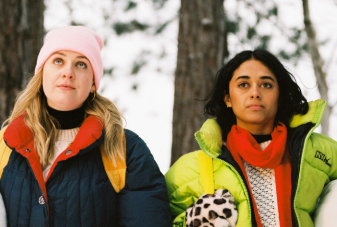 Two people wearing winter gear in the forest looking straight ahead.