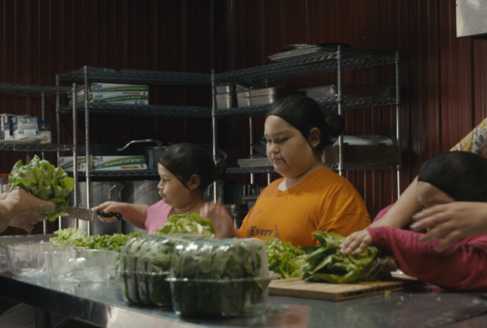 Children wearing hairnets preparing food on a large table.